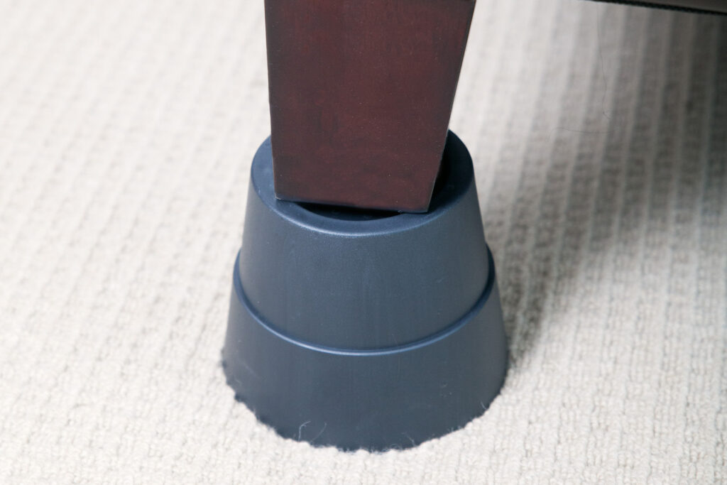 A grey Stander Furniture Riser under a brown chair leg.