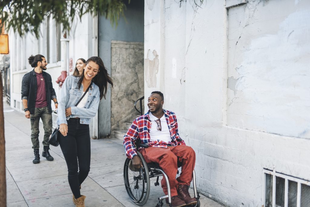 Young man in wheelchair with friend to right walking in town