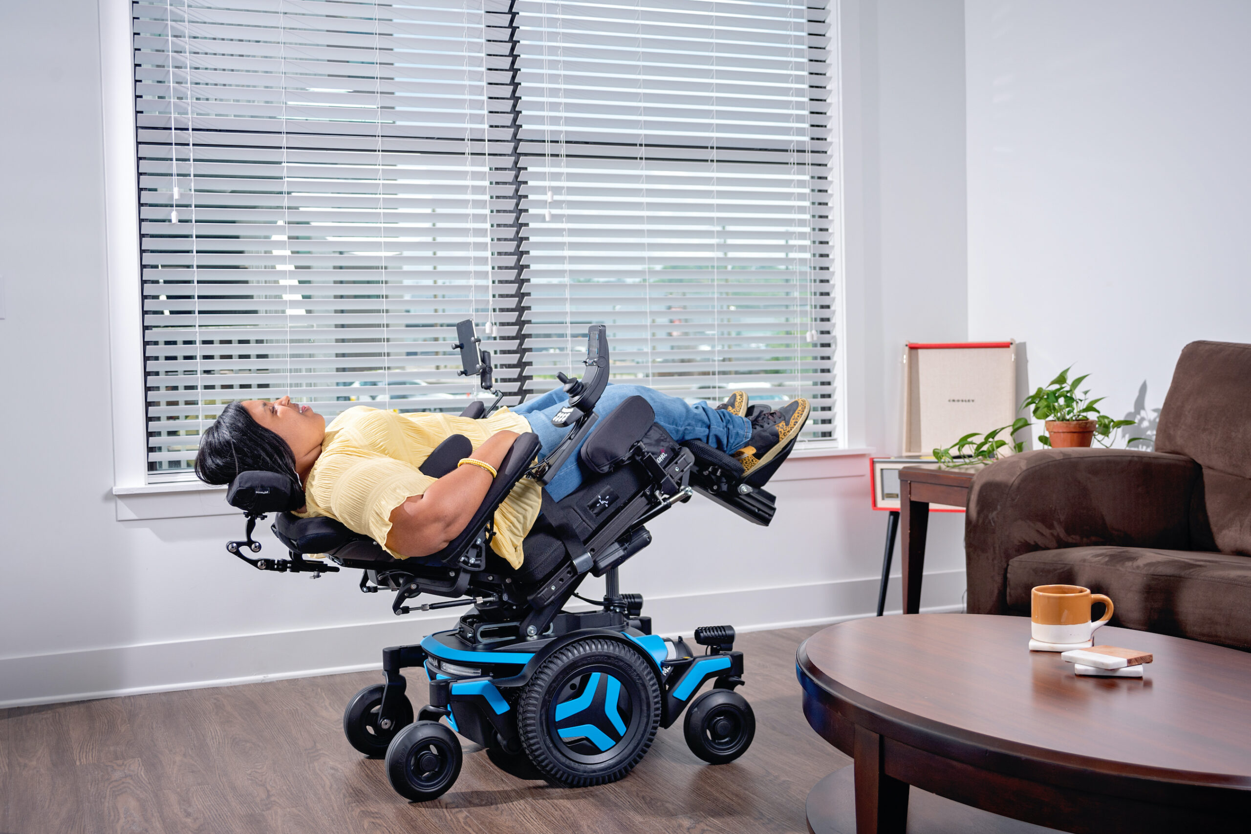 Young women in recline position in power wheelchair in a living room setting. 