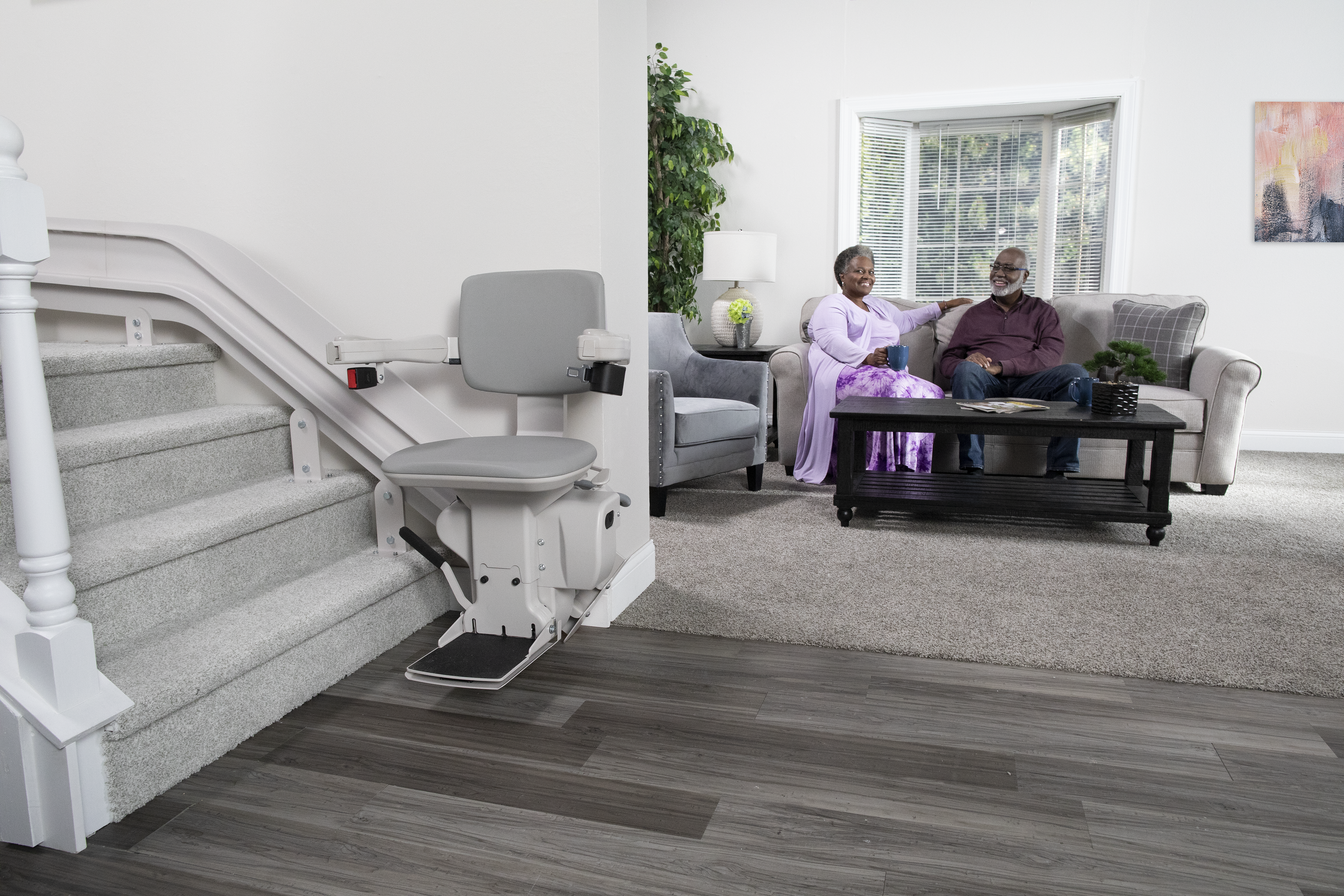 Man and woman seated on couch in background with stairlift in foreground